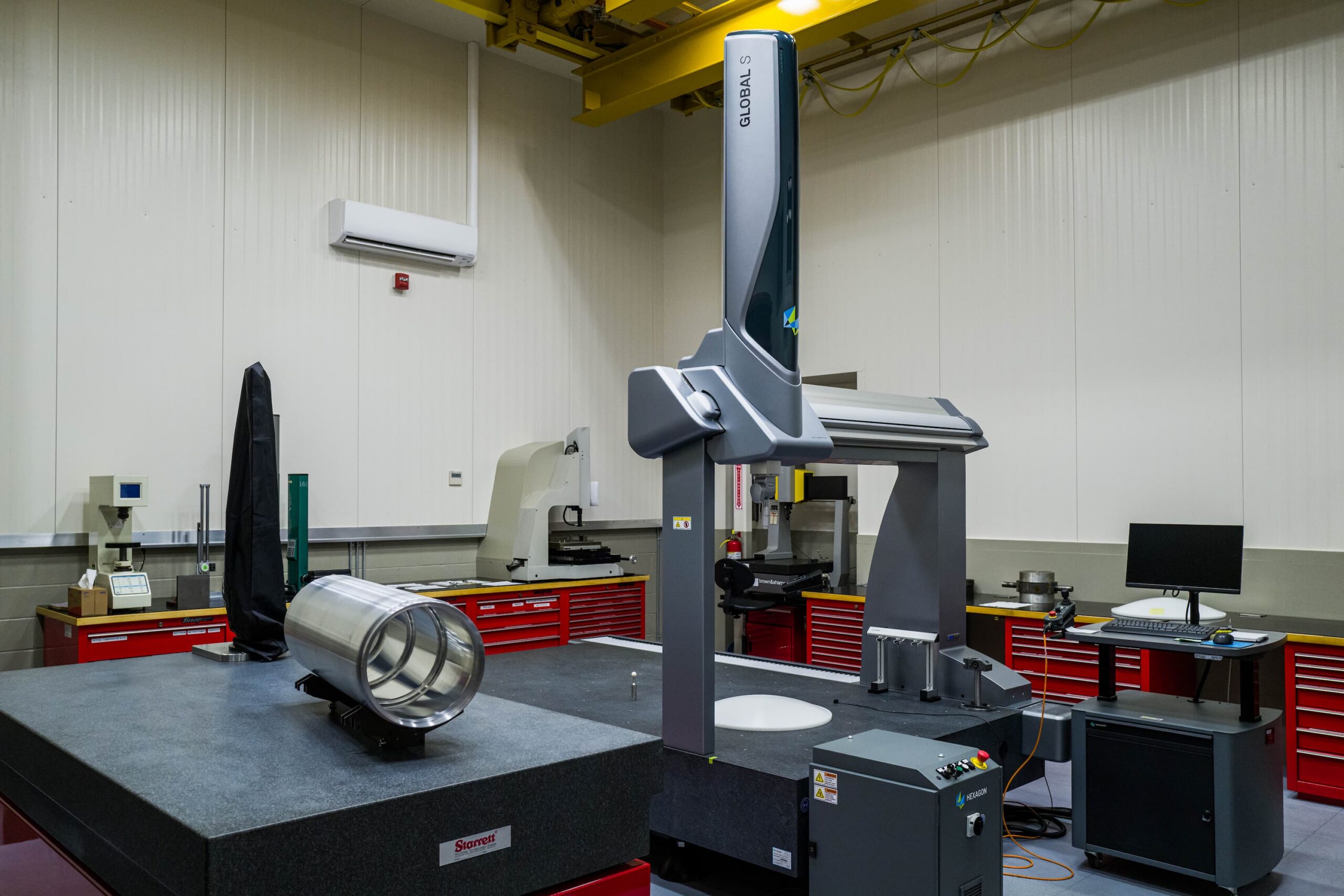 A machine positioned in a room featuring a table and another machine, highlighting a workspace environment.