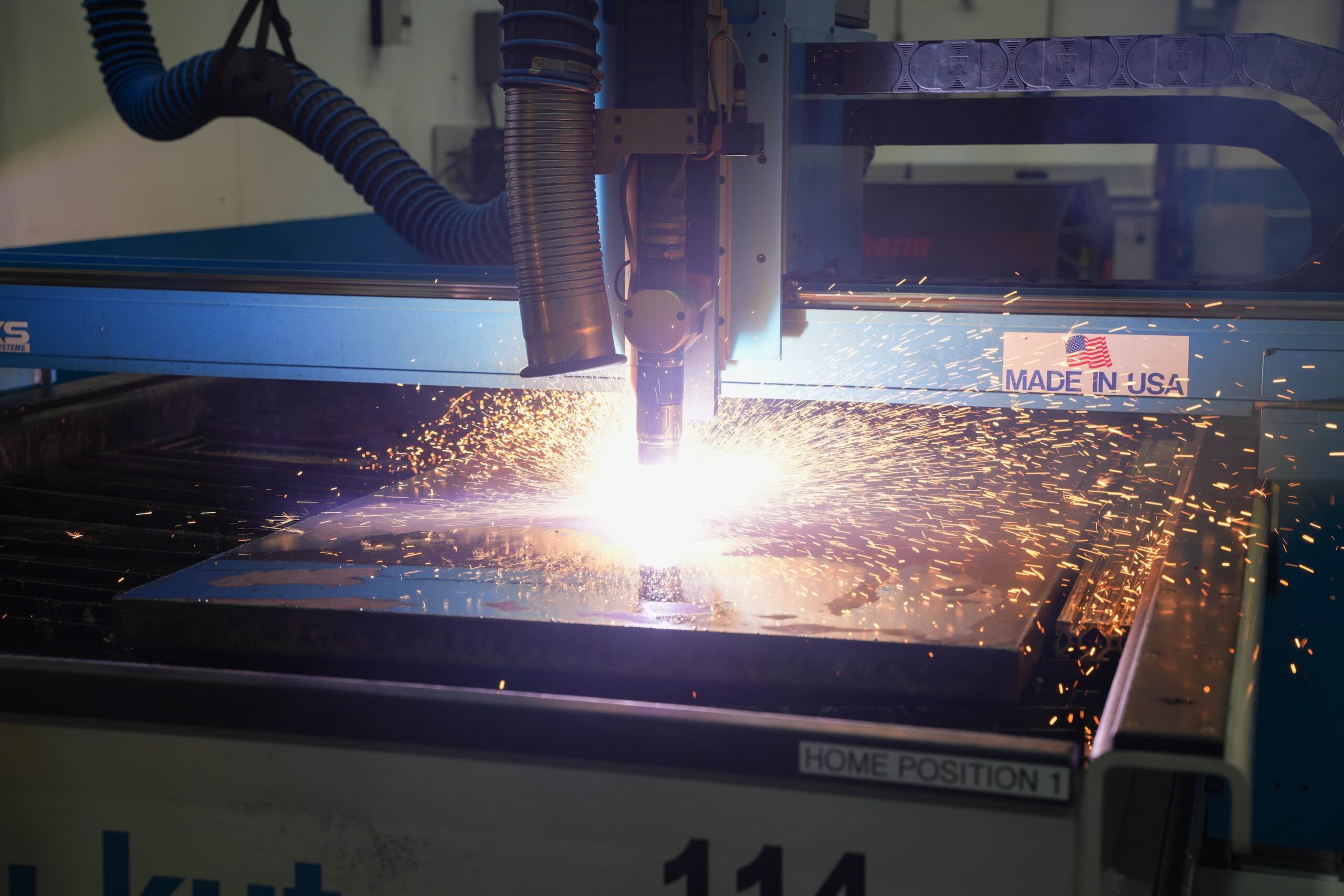 A machine using a plasma torch to cut through a sheet of metal, emitting bright sparks and intense light.